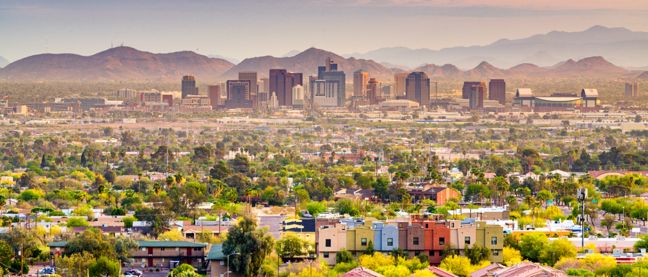 A scenic view of Phoenix, AZ, with downtown skyscrapers, suburban neighborhoods and surrounding desert mountains at sunset, highlighting the importance of asking the right questions before renting in Phoenix.