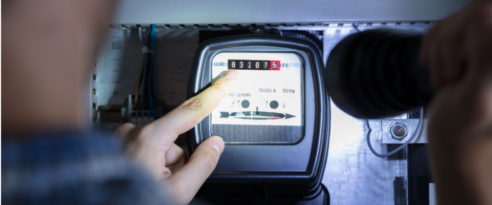 Person reading an electricity meter with a flashlight, representing accurate energy tracking and management in utility billing.
