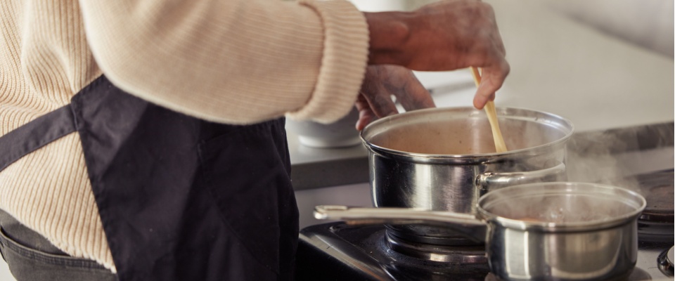 Person wearing an apron stirring food in a pot on a stovetop, demonstrating careful cooking practices and awareness of kitchen safety.