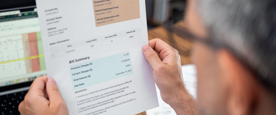 Man holding and reviewing a printed energy bill summary, showing detailed charges and costs related to utility billing.
