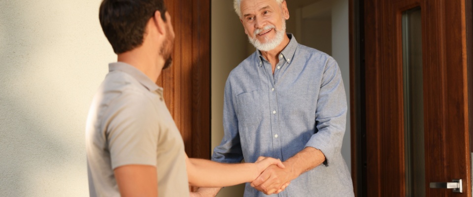 Smiling neighbors shaking hands at the front door, demonstrating how positive communication is key in resolving conflicts with neighbors.