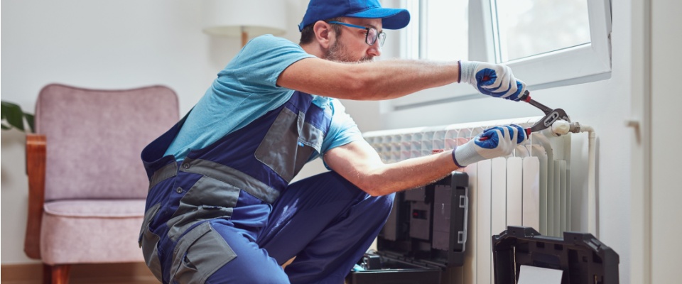 Maintenance worker fixing a radiator inside an apartment, addressing heating issues that can make a unit uninhabitable.
