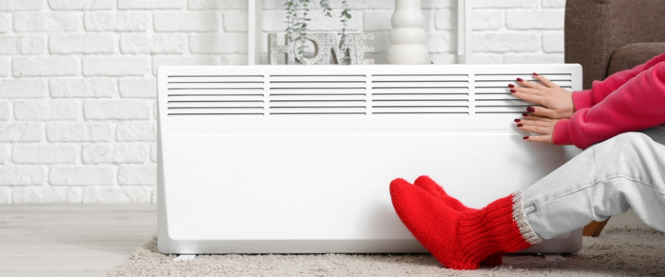 Person warming hands and feet near a home heater — highlighting the importance of understanding heating systems and costs in apartments in Ann Arbor, MI.
