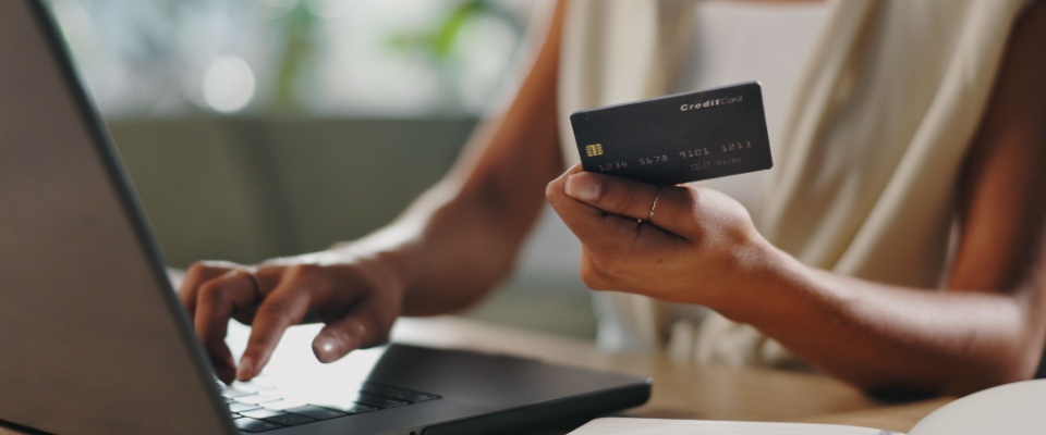A woman holding a credit card in front of a laptop to illustrate the fees for an online rental application.