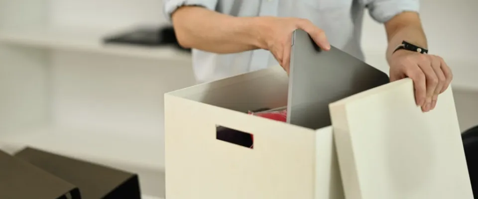 A young office employee packs his belongings into a box after a lease break, symbolizing an unexpected transition and the challenges of starting anew.