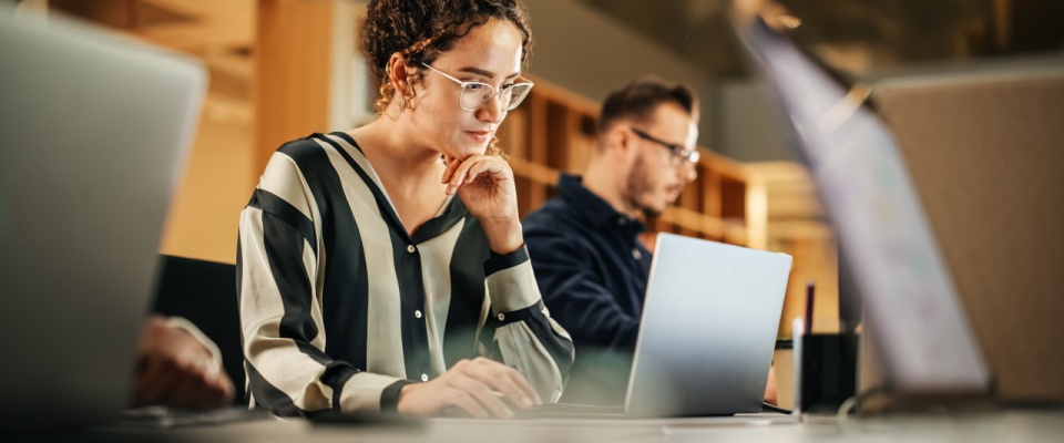 A cheerful young professional working confidently at her computer in a bright office, symbolizing the communication and coordination often needed during a lease break process between tenants and property managers.