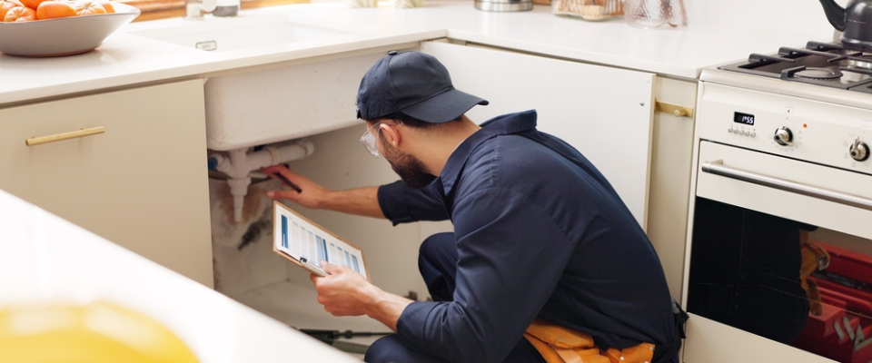Plumber performing apartment maintenance in a residential kitchen — reminding renters to ask landlords about plumbing, repairs, and upkeep before renting apartments in Huntsville, AL.