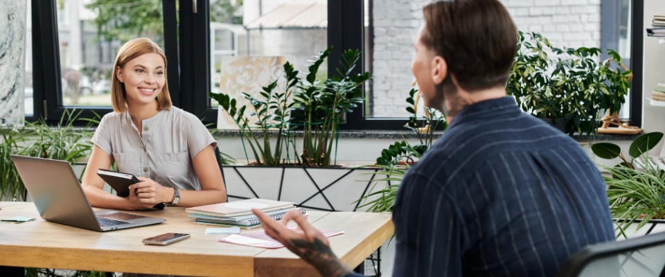 Two young professionals sharing ideas and collaborating in a bright, plant-filled workspace, illustrating teamwork and innovation, suitable for renting a space without a landlord reference.