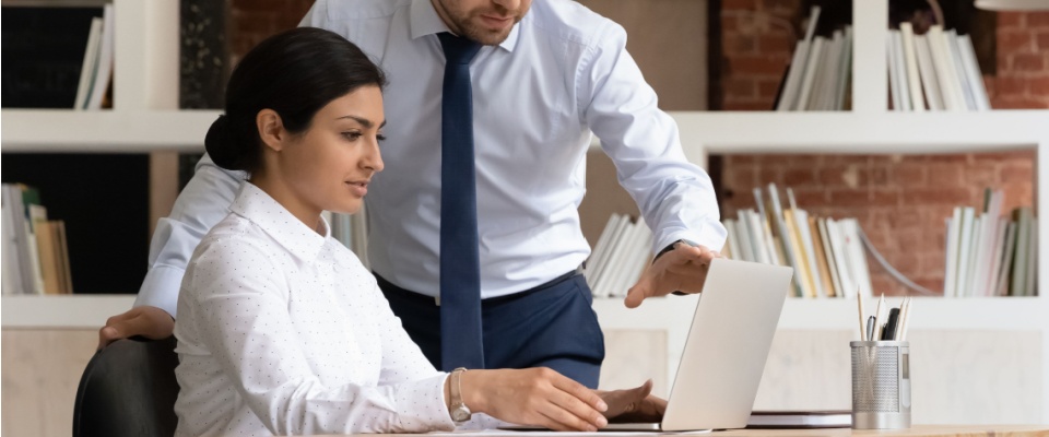 Young apprentice sitting at a desk with a laptop, receiving guidance from a colleague or mentor during an online corporate presentation, illustrating training and learning, suitable for renting a space without a landlord reference.