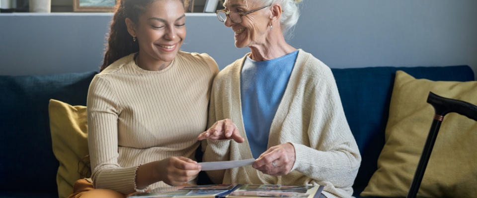 Younger woman helping an older woman look through a photo album, illustrating the potential impact of emotional downsizing for seniors.