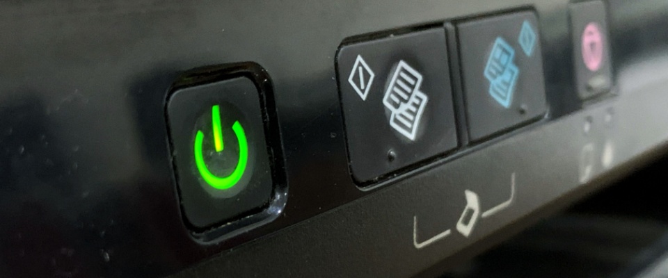 Close-up of a glowing green power button on an electronic device, representing standby power being used even when the device is idle.