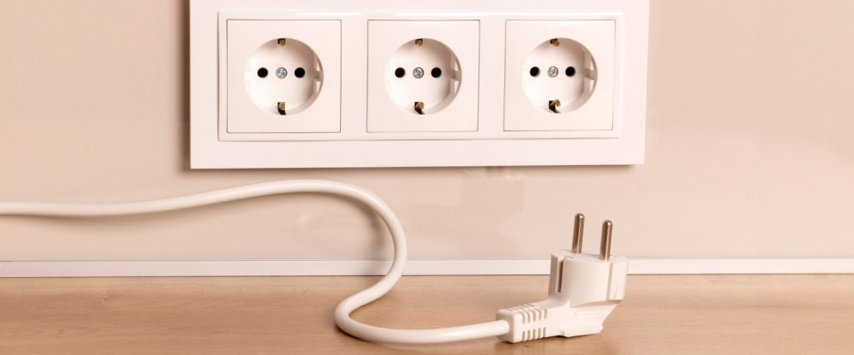 Unplugged power cord next to wall sockets, showing how to stop energy vampires by disconnecting devices that drain electricity in standby mode.