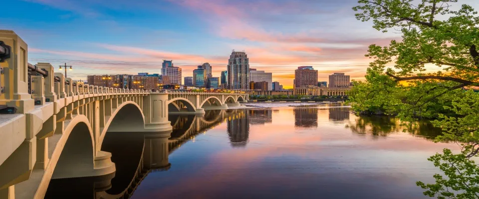 Minneapolis, Minnesota skyline along the Mississippi River with the Third Avenue Bridge at twilight, representing city housing activity and data for a renter engagement tracker.