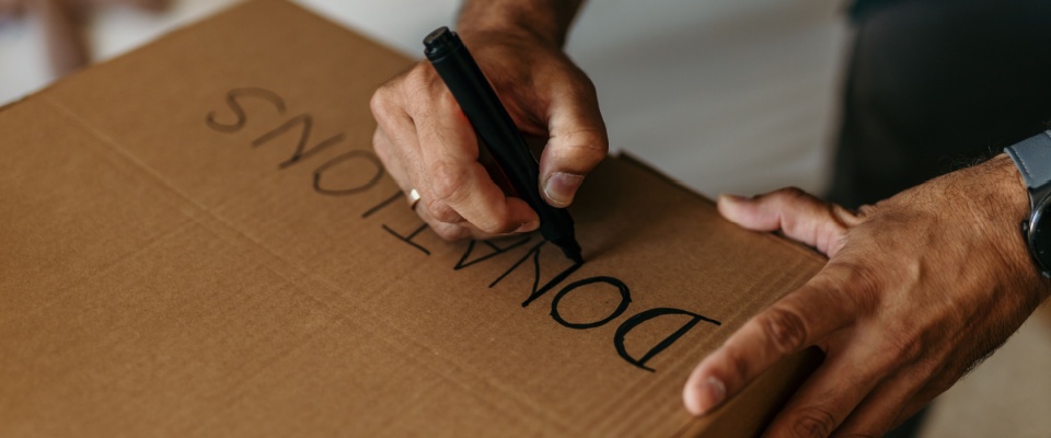 Person writing on a cardboard donations box, illustrating a useful downsizing tip for seniors—donating items before relocating.