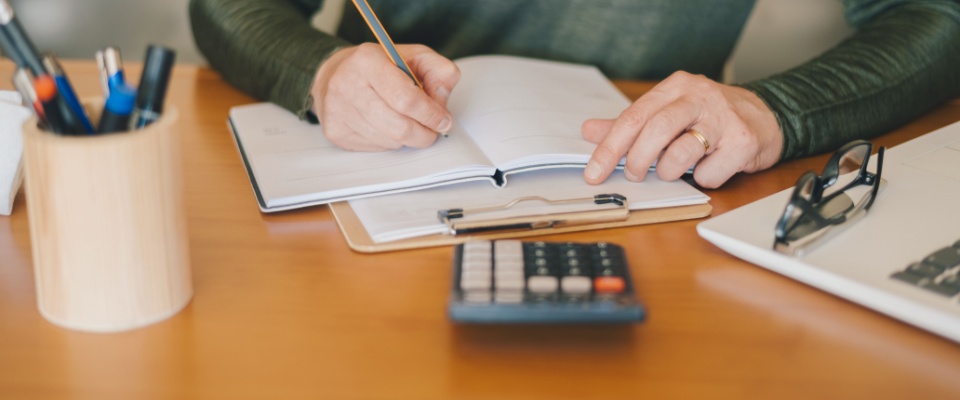 Focused woman managing household or business finances at a desk with bills, calculator, and laptop, representing the cost of living in Colorado Springs.
