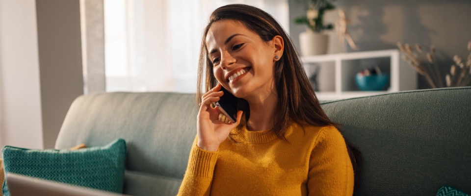 Portrait of a woman using laptop and a phone while sitting on couch at home.