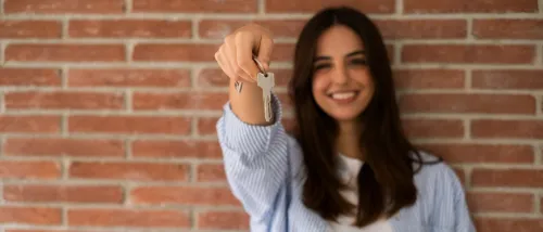 Smiling young woman holding house keys on moving day, representing the excitement and independence of a first-time renter.