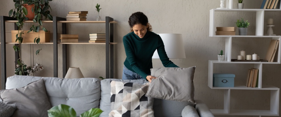 Happy young woman tidying up and organizing her modern living room during an apartment inspection, ensuring the home looks clean and comfortable.