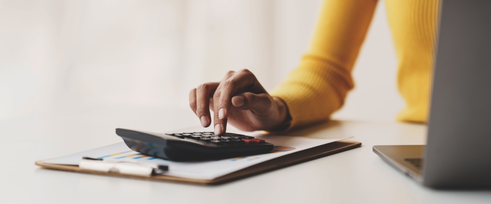Young woman using a calculator at a desk to review financial reports, representing budgeting and expense tracking for a first-time renter.