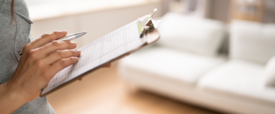 Close-up of a woman’s hand filling out a real estate appraisal form with a pen during an apartment inspection.