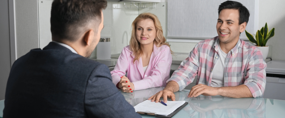 A couple sitting across from a leasing agent at a table, reviewing a written agreement, illustrating the importance of putting rent concessions and negotiated terms in writing.