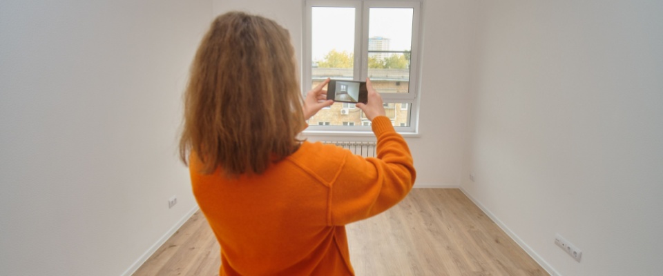 Woman taking a photo of an empty apartment room with her phone during an apartment inspection.