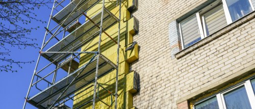 Scaffolding along the exterior of a brick property, illustrating an active apartment building renovation focused on insulation and structural upgrades.