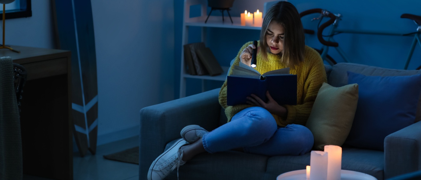 Woman reading a book using a flashlight and candles for light, showcasing useful things to have in your apartment during a power outage.