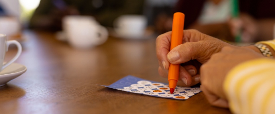 Apartment hunt bingo game concept illustrated by cropped hands of a senior woman playing bingo at a table.