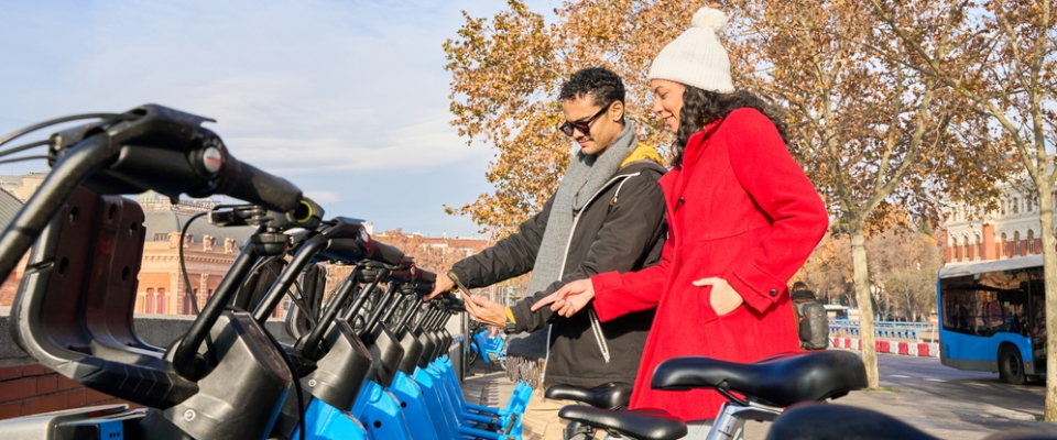 Two people unlock shared bikes at a bike-share station, highlighting a car-free transportation option that helps renters get around the city easily.