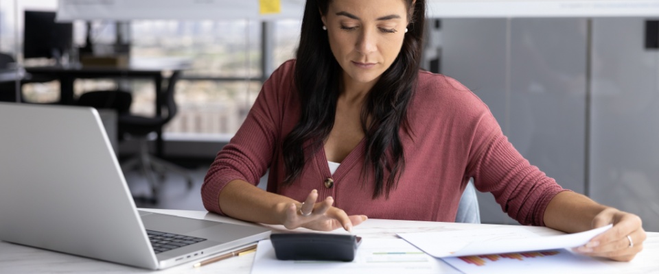 Woman reviewing bills and financial documents at her desk with a calculator, representing the cost of living in Omaha.