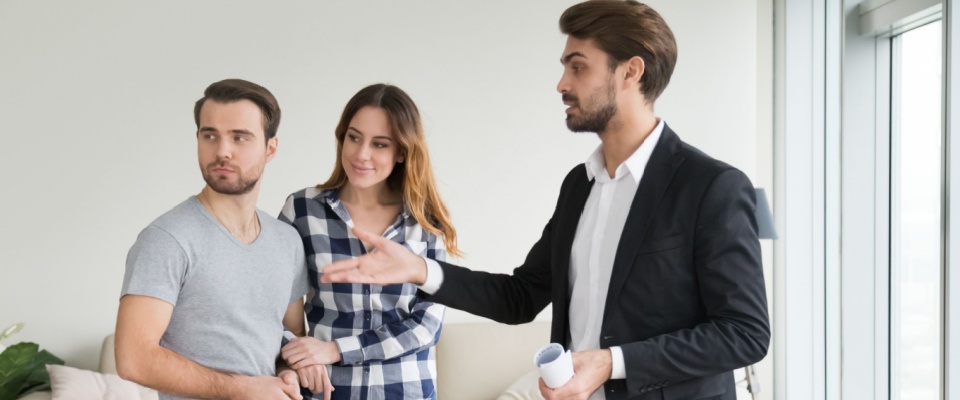 Real estate agent showing an apartment to a young couple, discussing rental terms and potential lease obligations.