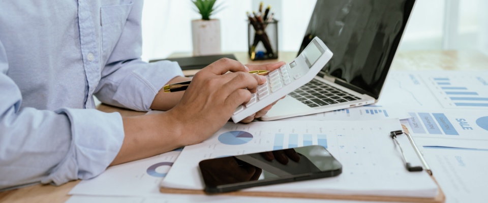 Asian businessman reviewing financial charts and reports on a laptop in a modern office, illustrating factors related to the cost of living in Harrisburg.