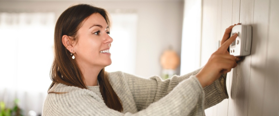 Happy woman adjusting a digital thermostat at home, managing energy use and comfort as part of renter resolutions.
