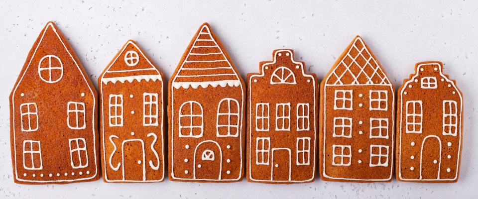Row of gingerbread cookies decorated to look like houses, arranged side by side on a light background in a festive holiday style.