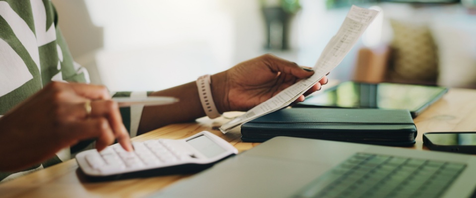 Renter resolutions concept showing a woman managing finances at home, using a calculator and laptop to review receipts, expenses, and budgeting documents.