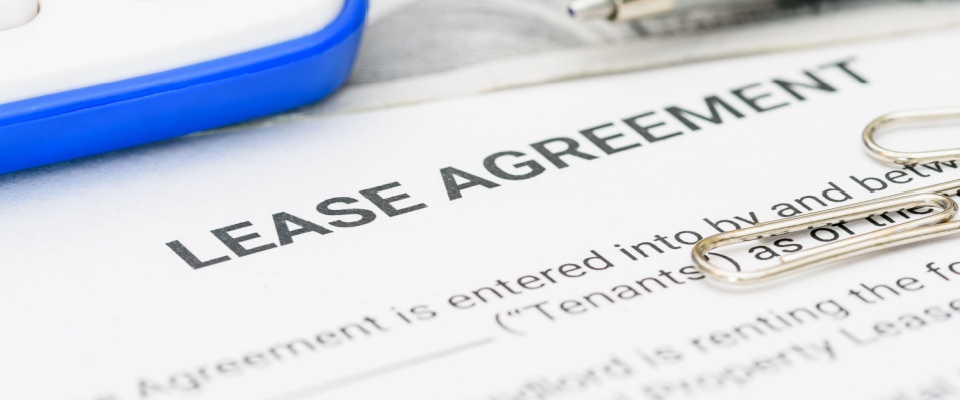 Lease agreement documentation and financial planning. A lease agreement, a calculator, pen, and paper clips, emphasizing financial calculations and legal preparations for rental or leasing contracts.