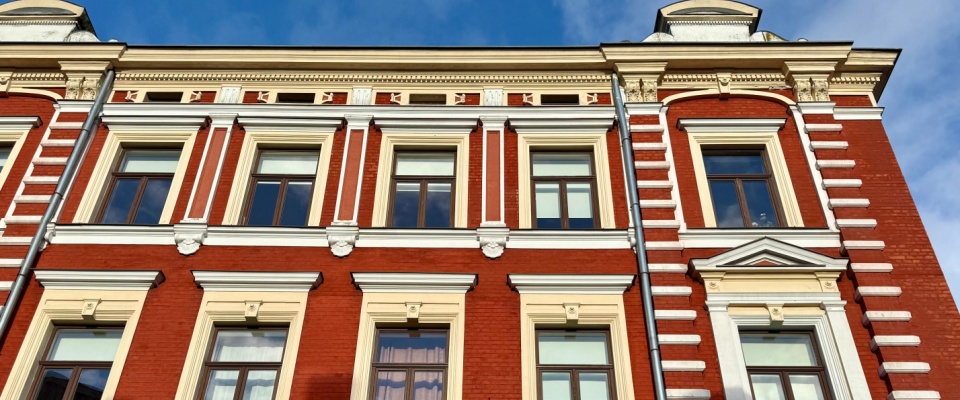 Historic property with an elegant red brick façade, ornate window frames, and classic architectural details, photographed in bright sunlight under a clear blue sky.