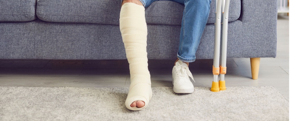 Renter sitting on a couch with a leg cast and crutches, illustrating how renters insurance coverage can help with liability and medical expenses after an accident.