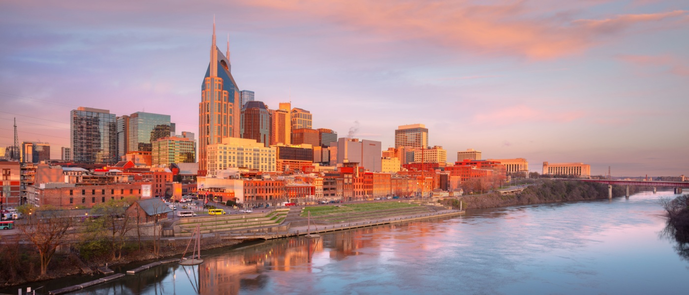 New apartments in Nashville featured in a sunrise view of the downtown Nashville skyline, reflected along the Cumberland River with modern buildings and a growing urban landscape.
