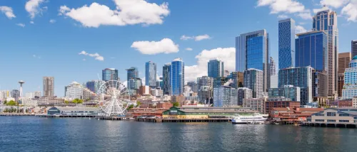 New apartments in Seattle highlighted by a bright, sunny panoramic view of the Seattle skyline from the water, featuring the iconic Space Needle and modern urban buildings under a clear blue sky.