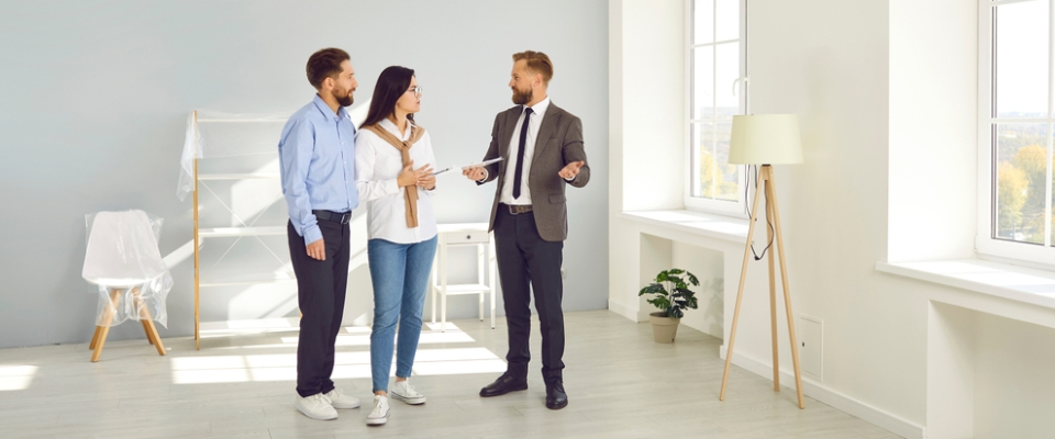 Renters touring an apartment in person with a leasing agent, discussing features inside a bright, unfurnished living space.