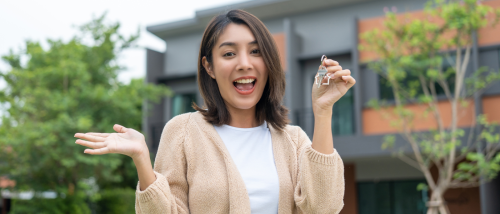Smiling renter holding apartment keys outside a modern apartment building, preparing to begin a self-guided apartment tour.