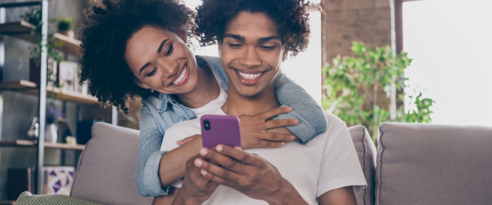 Happy couple reviewing options on a smartphone at home, illustrating how easy it is to sign up for renters insurance online.