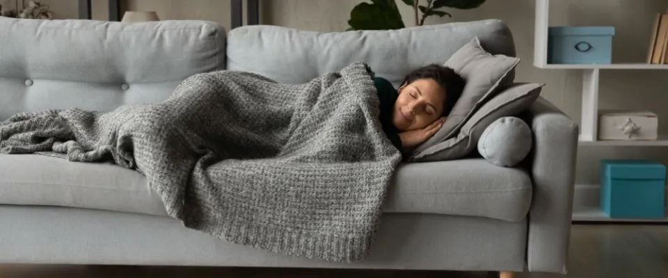 Peaceful woman resting under warm blanket on cozy couch in living room with closed eyes, sleeping or daydreaming, to illustrate quiet hours and quiet enjoyment.