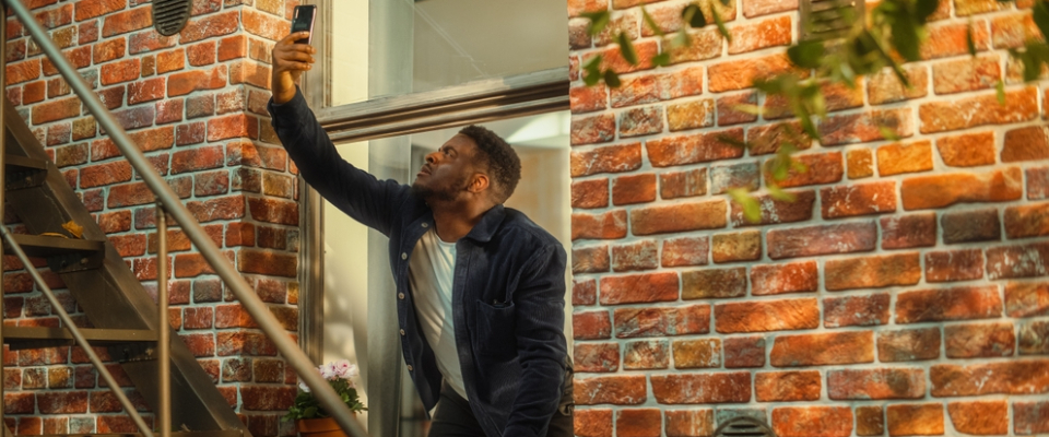 Man standing outside a brick apartment building holding up his phone to check signal—illustrating the importance of testing cell reception before renting apartments in Albany, NY.