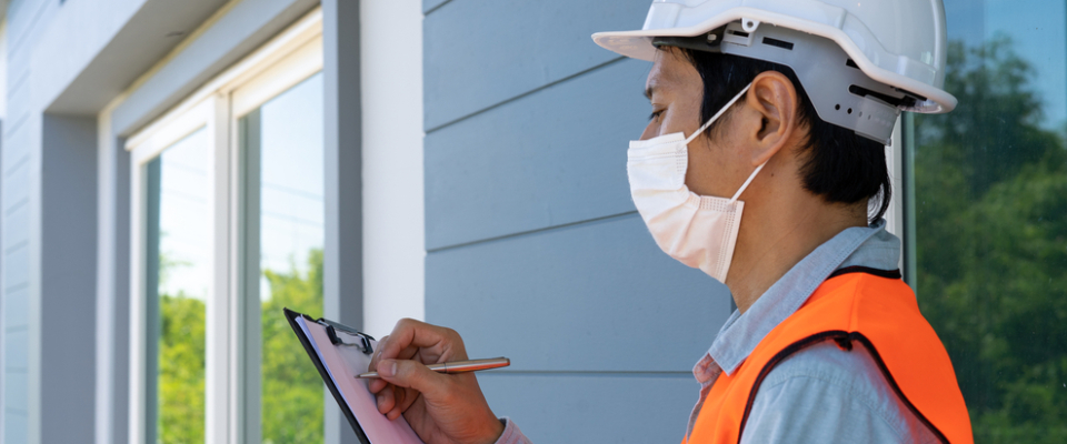 Inspector wearing a hard hat and safety vest reviewing paperwork outside a residential building—representing the importance of lead paint testing and certification when renting apartments in Albany, NY.