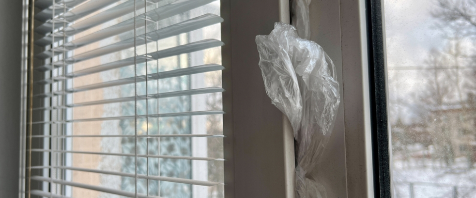 Close-up of an apartment window with blinds and plastic insulation covering the frame—illustrating why renters should ask about window quality and drafts before renting apartments in Albany, NY.