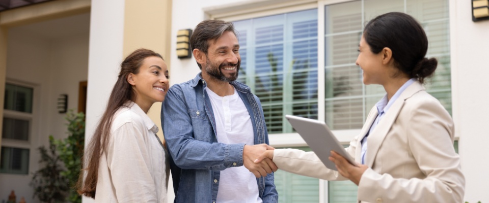 A couple made up of a man and a woman meet with a property manager in front of the apartment building to set up a lease renewal in the off-season for renting.