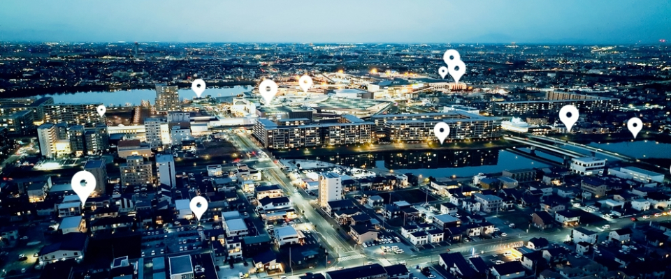 Aerial view of a city at night with location pins highlighting neighborhoods, representing how location impacts apartment budgeting and transportation costs.